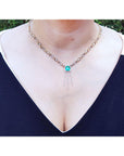 Kisses and hugs emerald necklace, square cut gemstone on a woman wearing a dark blue top.