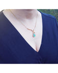 woman wearing a blue dress with a gold necklace featuring a teardrop emerald halo diamond pendant.