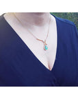 woman wearing a blue dress with a gold necklace featuring a teardrop emerald halo diamond pendant.