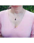 Person wearing a pink blouse with an opal necklace against a green outdoor background.