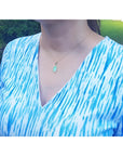 Ethiopian opal pendant with bluish-green hues, set in 14K yellow gold, worn on a woman's neck.