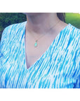 Ethiopian opal pendant with bluish-green hues, set in 14K yellow gold, worn on a woman's neck.