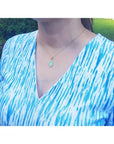 Ethiopian opal pendant with bluish-green hues, set in 14K yellow gold, worn on a woman's neck.