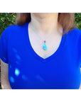 Vivid blue and white larimar teardrop pendant on a sterling silver necklace worn on a blue shirt.