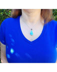 Vivid blue and white larimar teardrop pendant on a sterling silver necklace worn on a blue shirt.