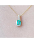 Emerald cut Colombian emerald pendant with halo diamonds on a 14K gold chain, worn on a neck.