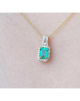 Emerald cut Colombian emerald pendant with halo diamonds on a 14K gold chain, worn on a neck.