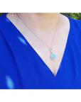 Ethiopian Welo opal and diamond pendant in 14K white gold, worn on a blue top.