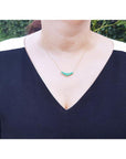 Woman wearing a 14K gold necklace with five round medium green Colombian emeralds.