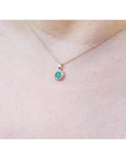Minimalist 14K yellow gold necklace with a round-cut Colombian emerald pendant surrounded by diamonds.