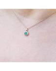 Minimalist 14K yellow gold necklace with a round-cut Colombian emerald pendant surrounded by diamonds.