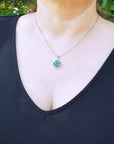 Woman wearing a black top with a round cut cluster emerald necklace, set within a delicate 4-leaf clover design