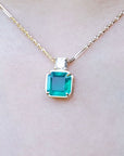 Front side of a yellow gold necklace with an Asscher cut emerald gemstone pendant on a light background