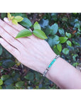 Hand wearing a bracelet with vibrant Colombian emeralds and princess cut diamonds.