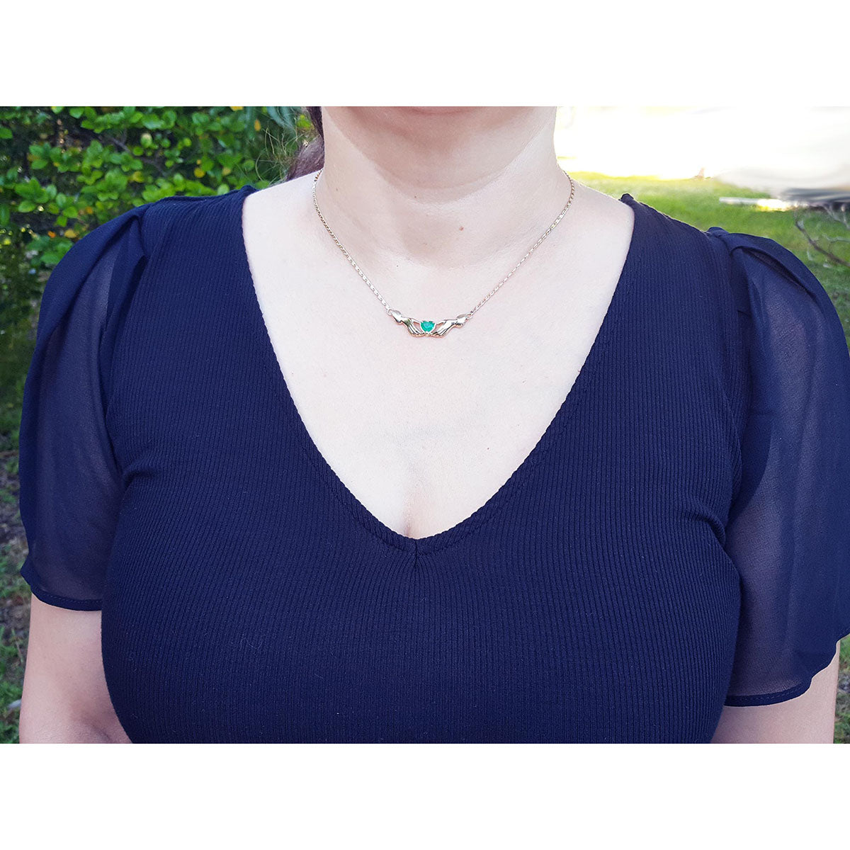 Woman wearing a blue top with puffed sleeves and a Claddagh emerald heart necklace outdoors.