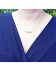 14K gold necklace with five round, medium light green Colombian emeralds of varying sizes.
