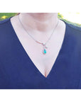 Woman wearing a blue dress with a white gold necklace featuring a natural emerald pendant in a halo diamond