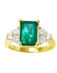 A women's emerald ring with accent side diamonds yellow gold topside view.