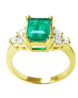 A yellow gold ring with a natural emerald and accent side diamonds, top and sides profile view.