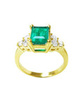 A yellow gold ring with a natural emerald and accent side diamonds, top and sides profile view.