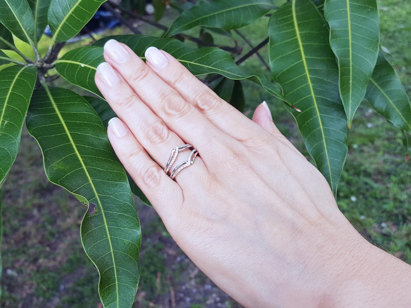 Hand wearing a diamond ring guard enhancer with green leaves in the background.