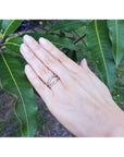 Hand wearing a diamond ring guard enhancer with green leaves in the background.