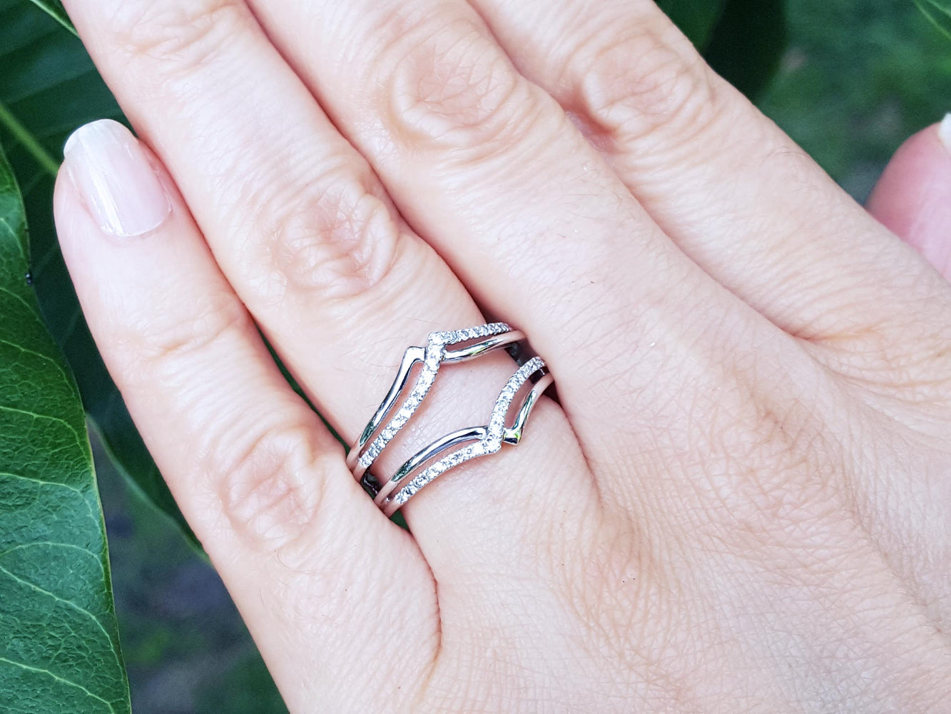 Hand wearing a wrap enhancer for solitaire rings on a blurred green background.