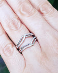 Hand wearing a wrap enhancer for solitaire rings on a blurred green background.