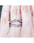 Close-up of a hand wearing a diamond ring guard enhancer wrapper 14k white gold with a blurred green background.