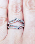 Close-up of a hand wearing a diamond ring guard enhancer wrapper 14k white gold with a blurred green background.
