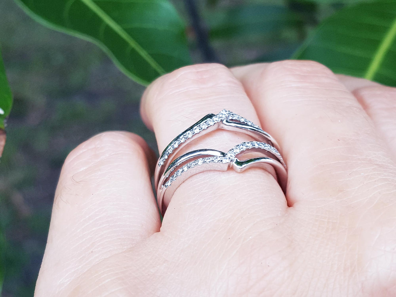 White gold wrapper natural diamonds enhancer ring on a finger with a blurred green leafy background.