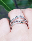 White gold wrapper natural diamonds enhancer ring on a finger with a blurred green leafy background.