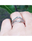 White gold wrapper natural diamonds enhancer ring on a finger with a blurred green leafy background.