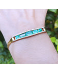 Gold bracelet with vife genuine emeralds on a wrist against a blurred green background.