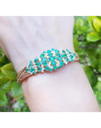 14K yellow gold bangle with round Colombian emeralds and diamonds in a floral design.