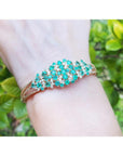 14K yellow gold bangle with round Colombian emeralds and diamonds in a floral design.