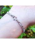 White gold bracelet with diamonds on a wrist with a blurred green background.