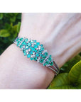14k white gold bangle bracelet with round Colombian emeralds and diamonds on a wrist.