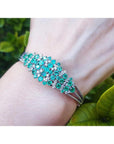 14k white gold bangle bracelet with round Colombian emeralds and diamonds on a wrist.
