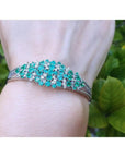 14k white gold bangle bracelet with prong-set round Colombian emeralds and diamonds on a wrist.