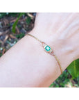 On women's wrist natural emerald solitaire bracelet crafted in 14k yellow gold against a natural background.