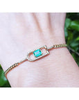 14K yellow gold bracelet with a square emerald-cut Colombian emerald and diamond accents on a wrist.