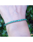 A natural colombian emerald tennis bracelet on a wrist against a blurred green background.