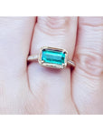 Hand wearing a natural emerald ring east west orientation prong set in yellow gold.