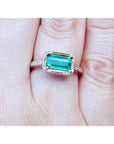 Hand wearing a natural emerald ring east west orientation prong set in yellow gold.