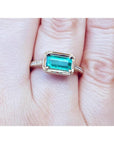 Hand wearing a natural emerald ring east west orientation prong set in yellow gold.