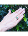 A hand's person wearing a natural colombian emerald ring on a green leafy background.