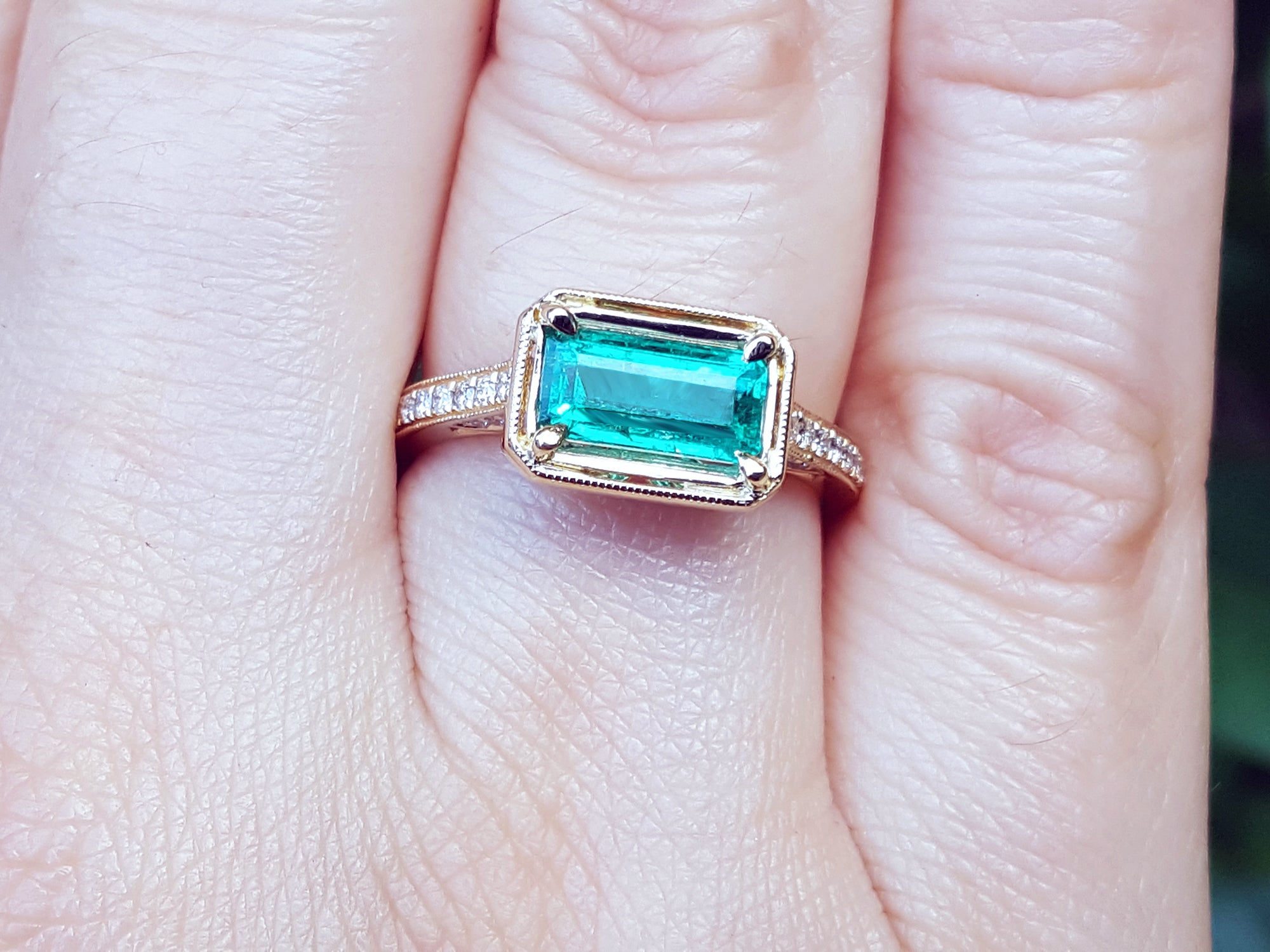 Hand wearing a natural emerald ring east west orientation prong set in yellow gold.