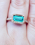 Hand wearing a natural emerald ring east west orientation prong set in yellow gold.