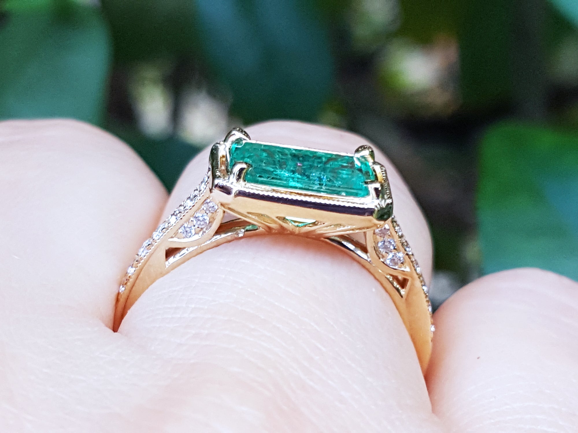 The underside view of a colombian emerald ring in yellow gold on a finger.